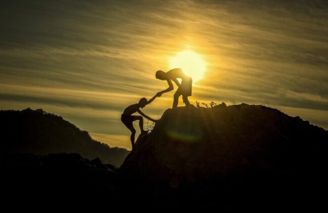 Silhouette of person helping another climb