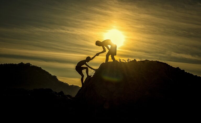 Silhouette of person helping another climb